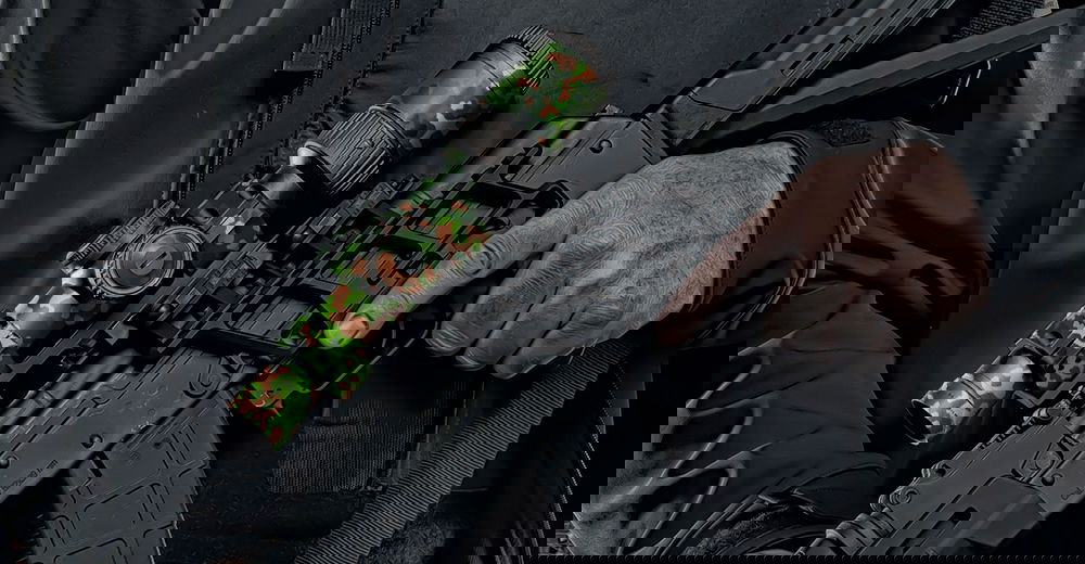 Mann hält Airsoft-Gewehr mit Tarnmuster-Zielfernrohr in Nahaufnahme.