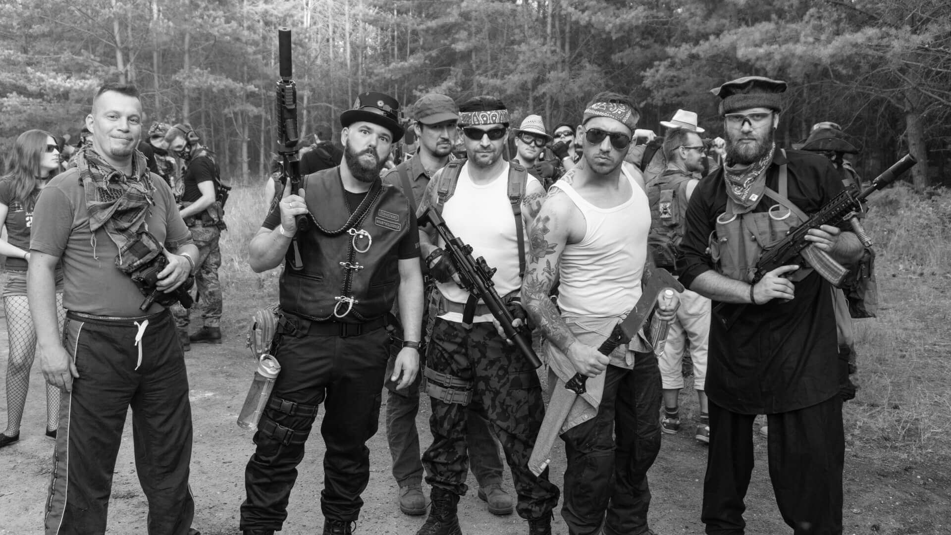 Gruppe von Airsoft-Spielern im Wald, teils mit Gewehren, in taktischer Ausrüstung und legerer Kleidung.