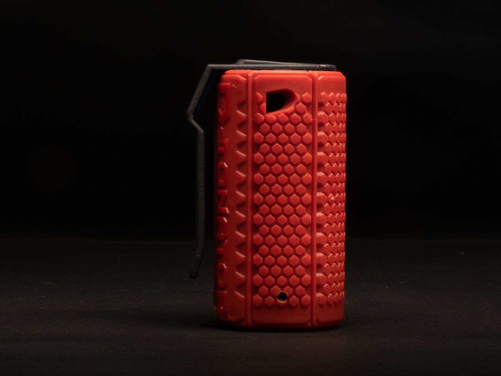 Rote Airsoft-Granate mit Wabenmuster, schwarzer Sicherheitsbügel auf dunklem Hintergrund.
