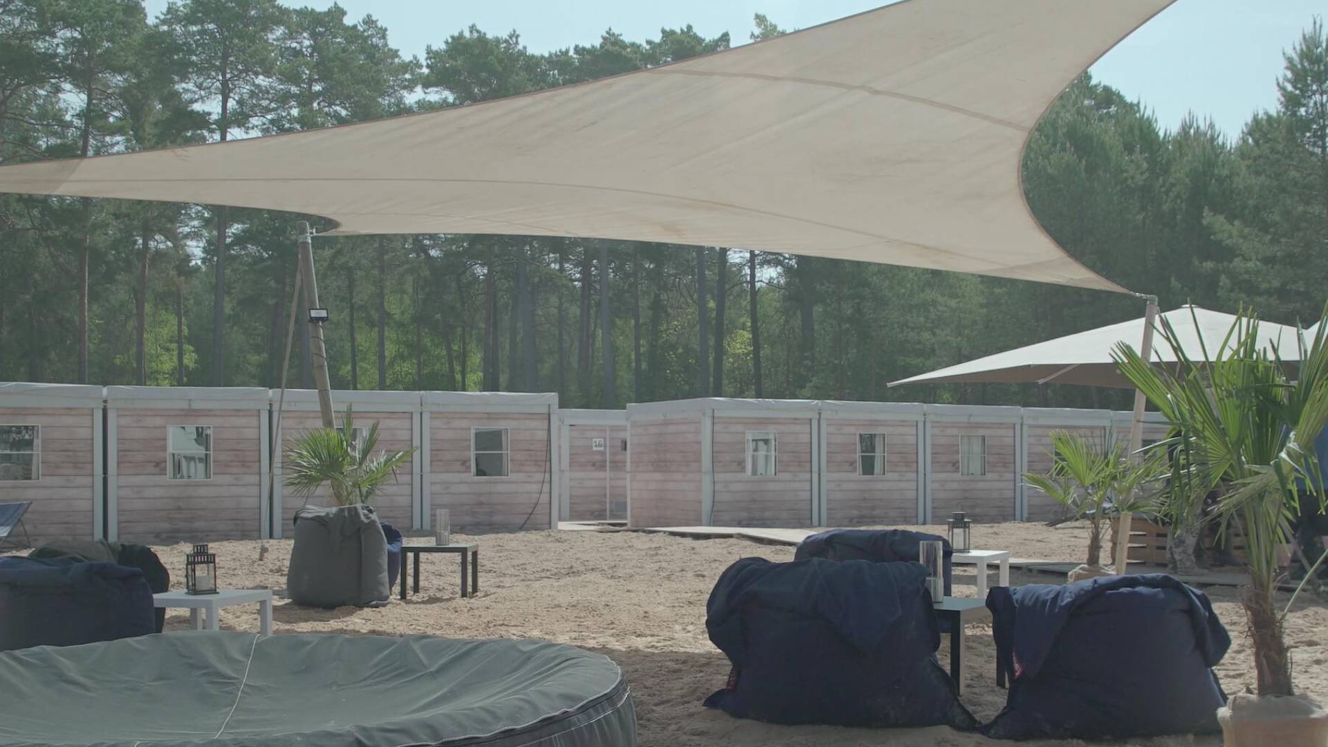 Outdoor-Ruhebereich mit Sitzsäcken und Sonnensegel vor Holzwänden im Wald.