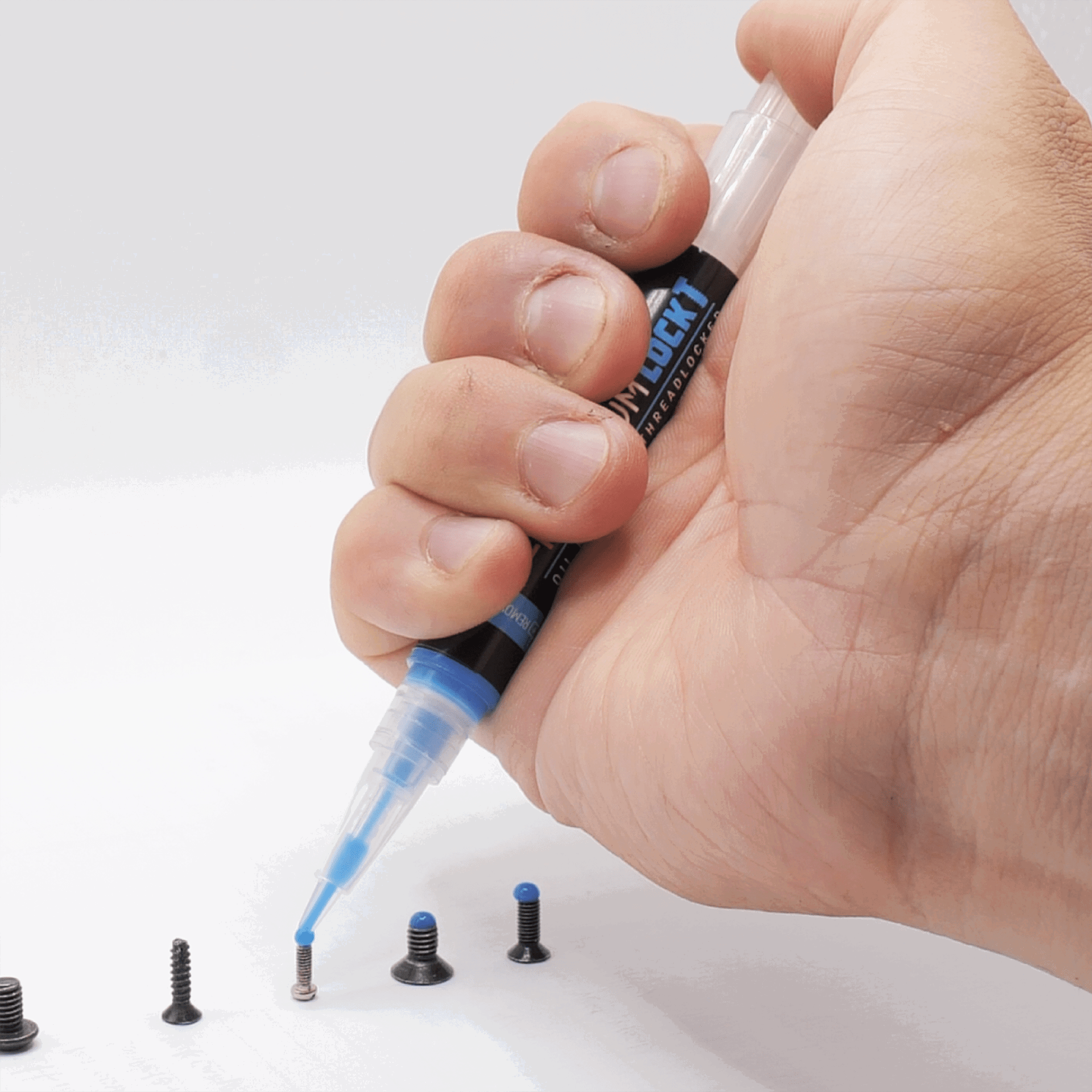 Hand trägt blauen Kleber auf eine kleine Schraube auf. Weitere Schrauben liegen daneben.