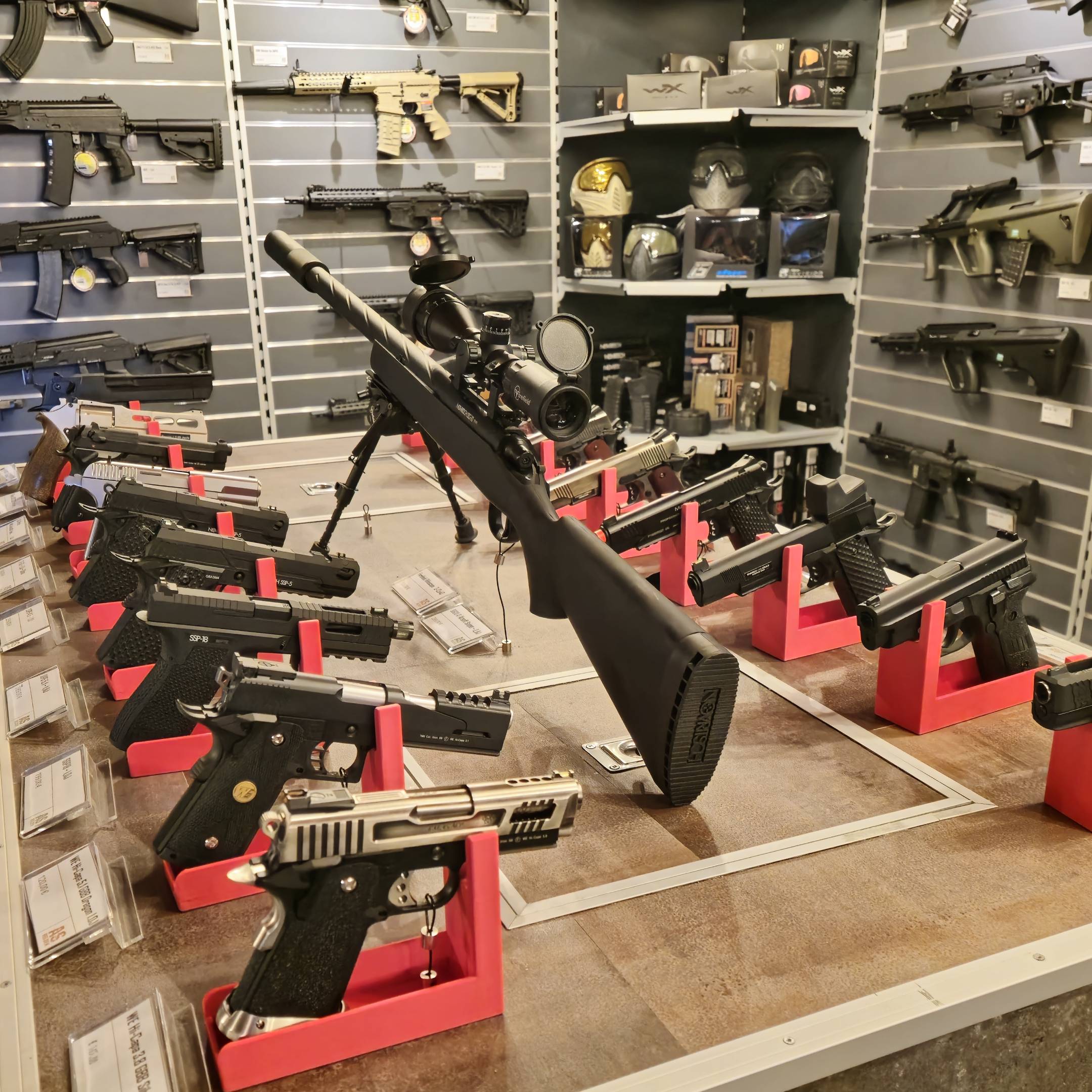 Airsoft-Waffen in roter Ausstellung: Pistolen, Gewehre und Zubehör in einem Ladenregal.