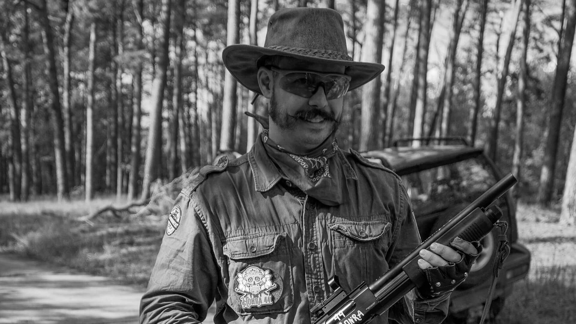 Person mit Cowboyhut, Schutzbrille und Airsoft-Gewehr im Wald.