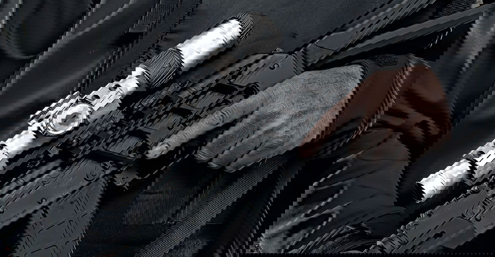 Person hält Airsoft-Gewehr mit Zielfernrohr in dunkler Ausrüstung.