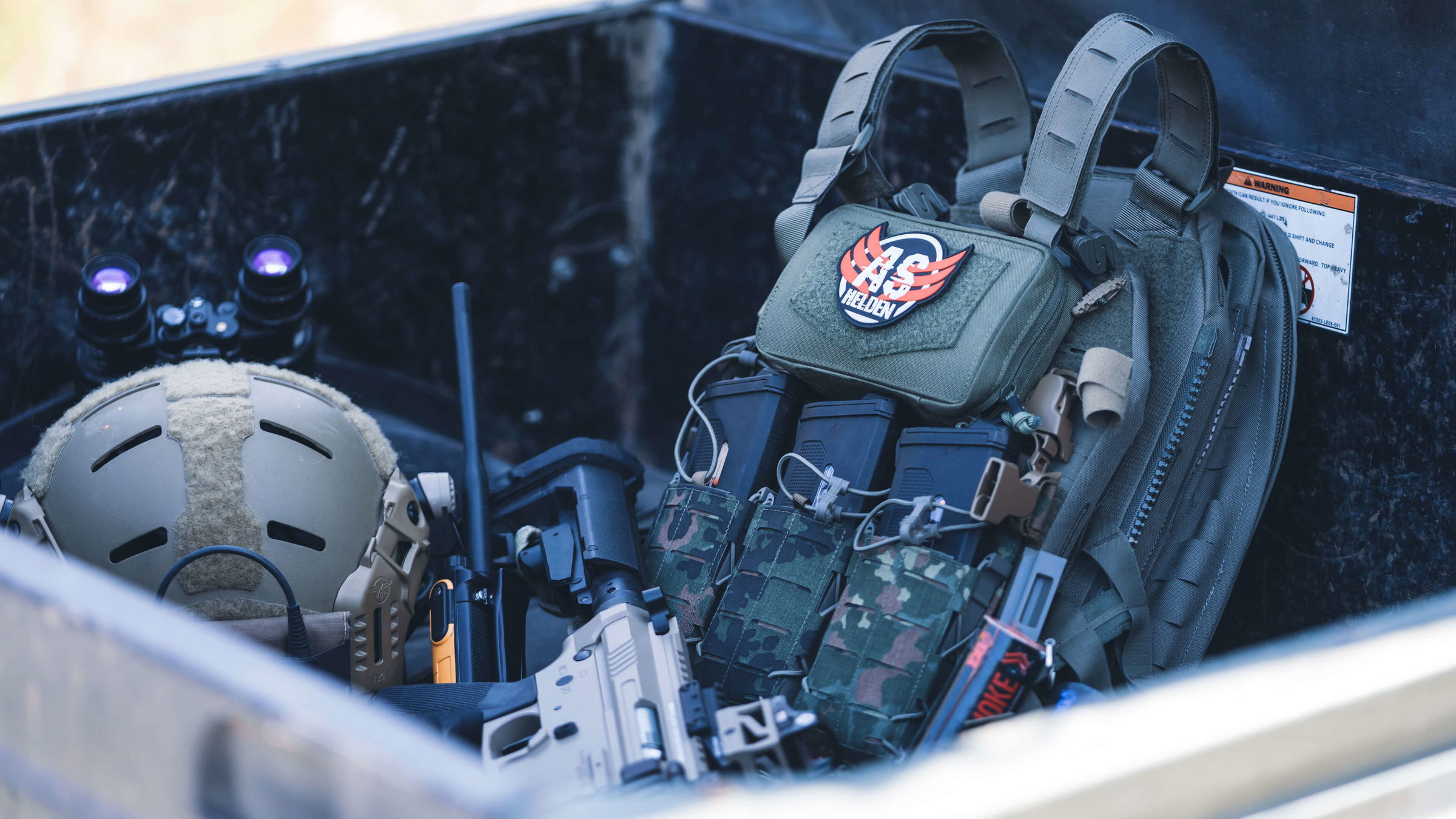 Helm, taktische Weste und Airsoft-Markierer in einer Kiste, bereit für das nächste Airsoft-Spiel.