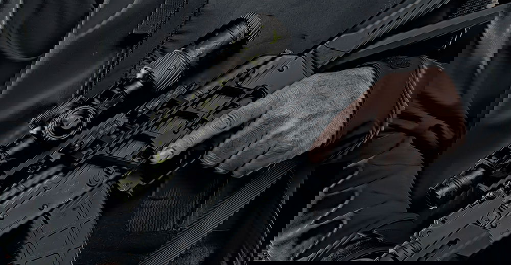 Person hält ein Airsoft-Gewehr mit Zielfernrohr in dunkler Kleidung.