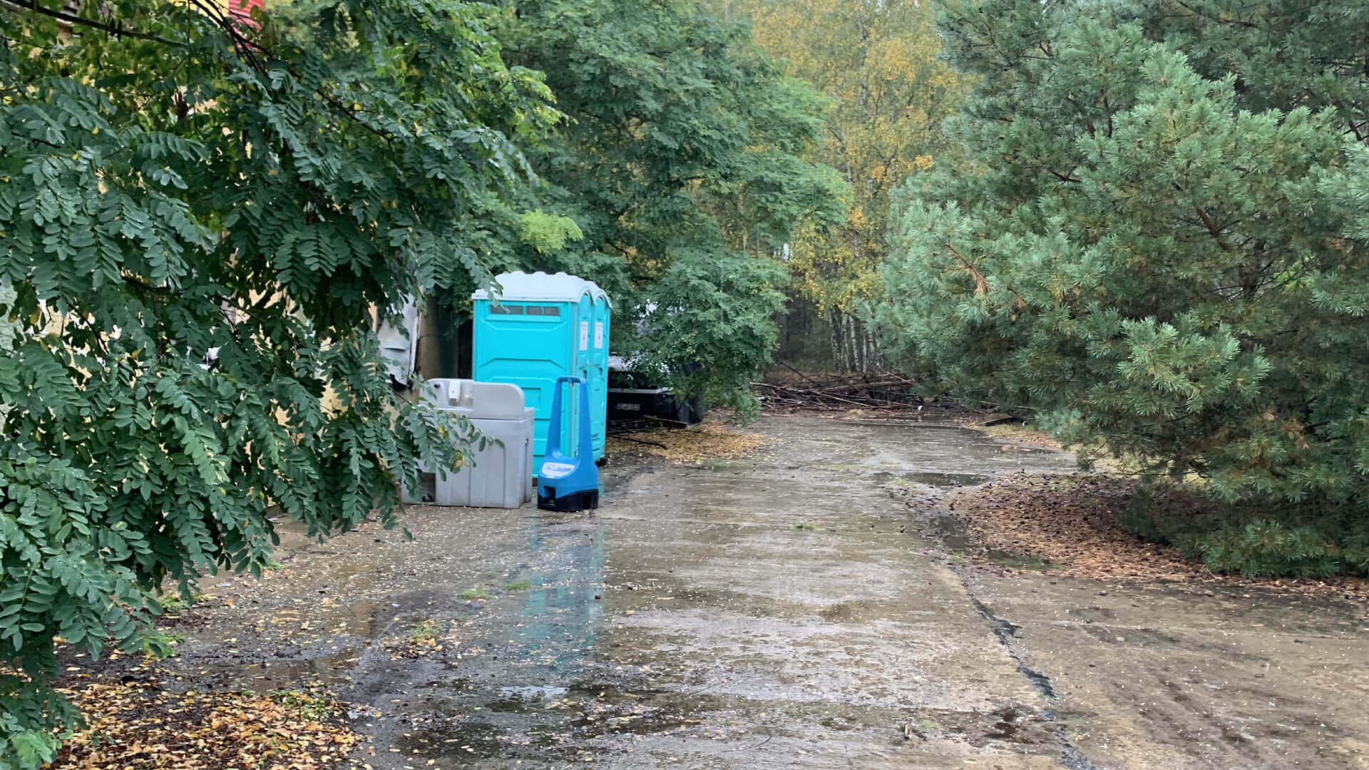 Grüne Landschaft mit einem blauen mobilen WC und Waschstation am Wegesrand.