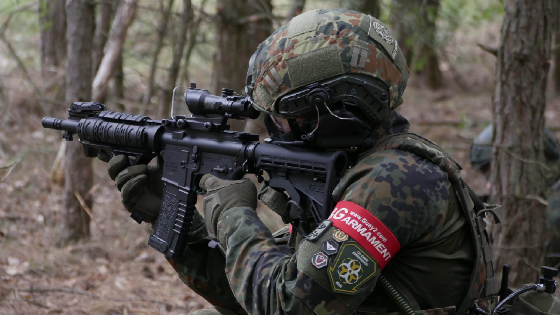 Airsoft-Spieler in Tarnkleidung zielt mit Airsoft-Gewehr im Wald.