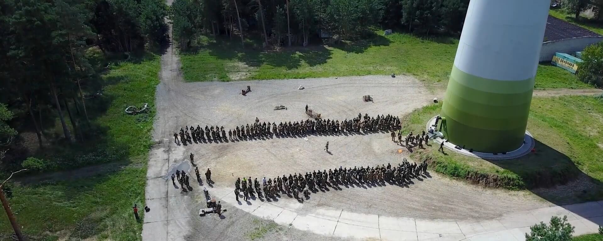 Luftaufnahme großer Airsoft-Gruppe in Feldformation bei Wald und Windrad.