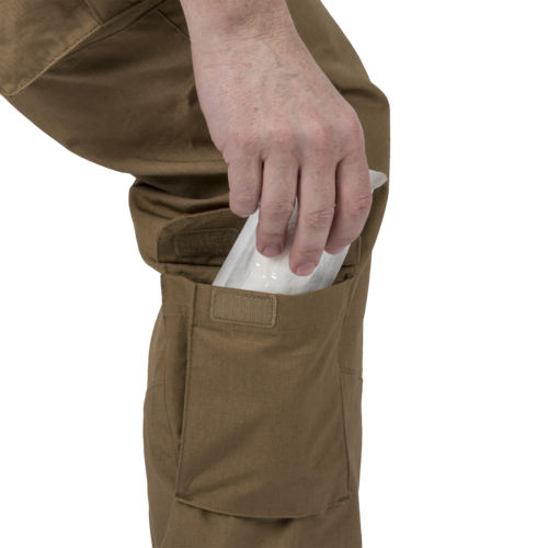 MBDU® Trousers - NyCo Ripstop - MultiCam Black™ Hand steckt einen Gegenstand in die Beintasche einer braunen Cargohose.
