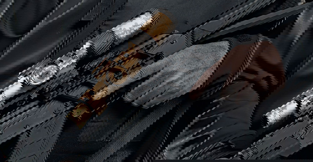 Person hält Airsoft-Gewehr mit Tarn-Visier in der Hand, Nahaufnahme.