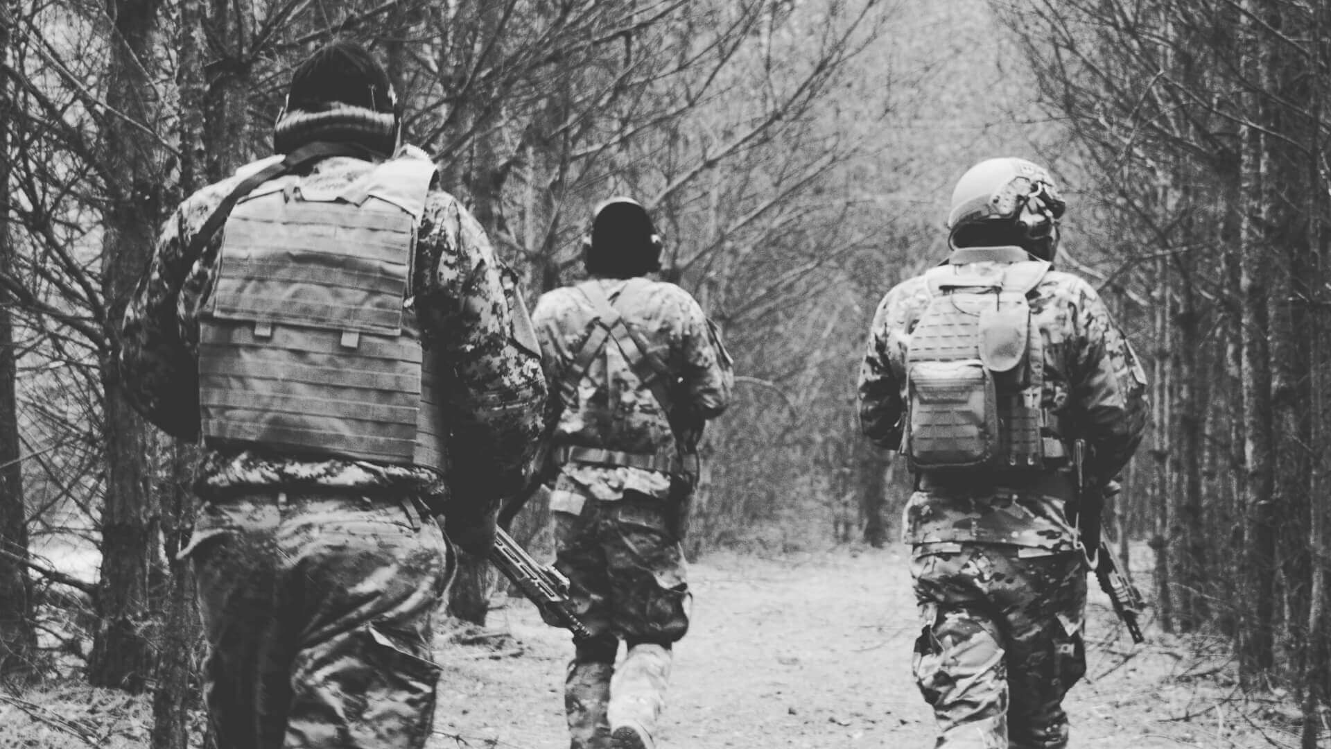 Drei Airsoft-Spieler in Tarnkleidung laufen durch einen Wald.