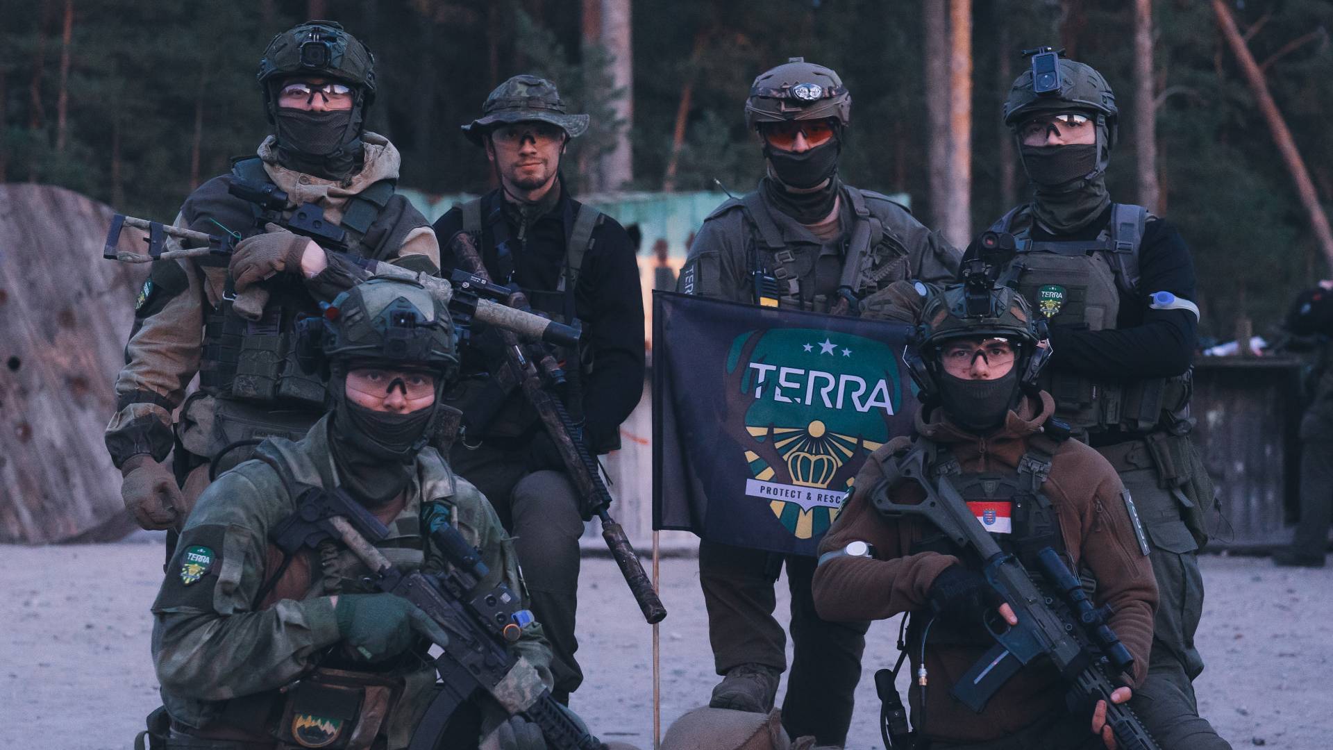 Airsoft-Team in taktischer Ausrüstung, posiert mit "TERRA"-Flagge in bewaldetem Gelände.