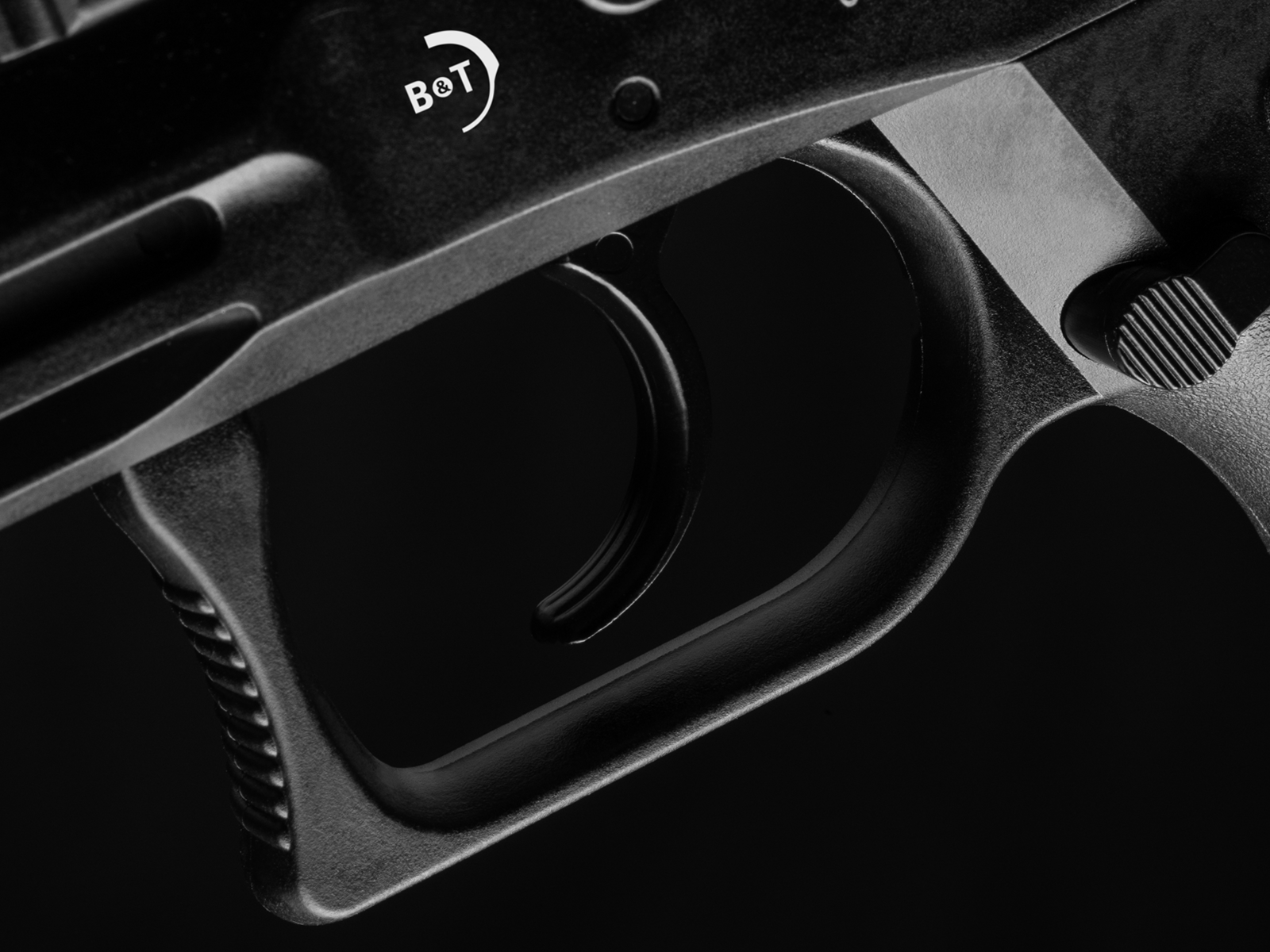 Nahaufnahme eines schwarzen Abzugs mit "B&T" Logo, Detail einer Airsoft-Waffe.