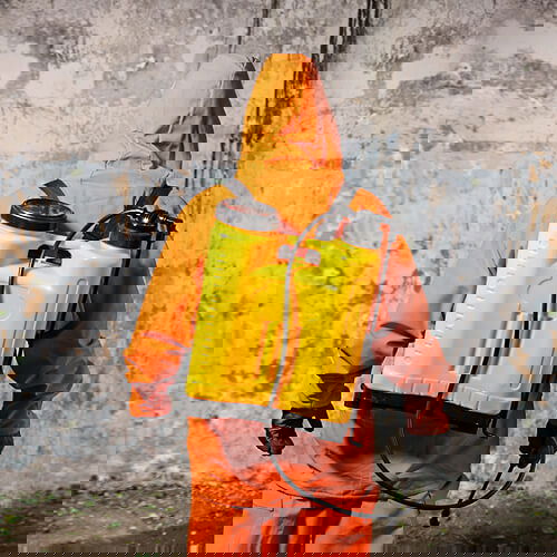 Person in orange Schutzanzug mit gelbem Sprühgerät an der Wand.