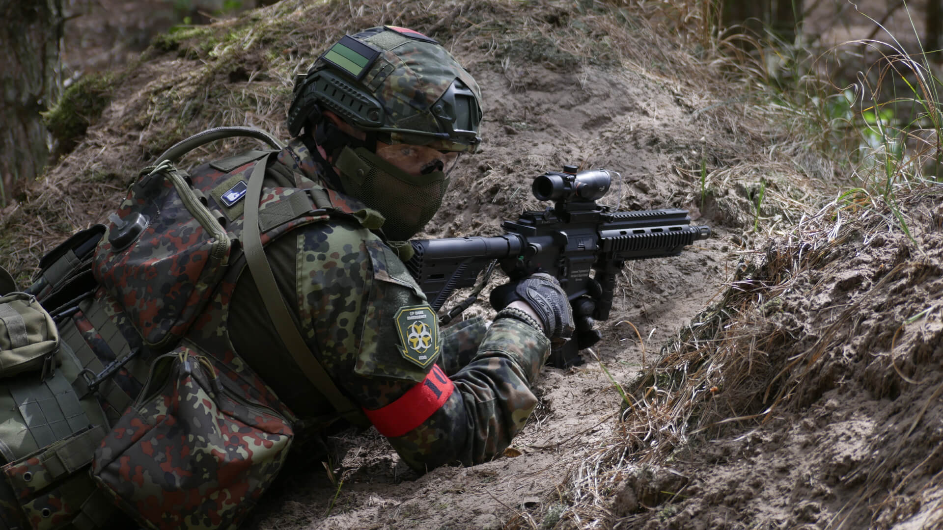 Airsoft-Spieler in Tarnkleidung mit Gewehr in Waldumgebung, liegend im Hinterhalt.