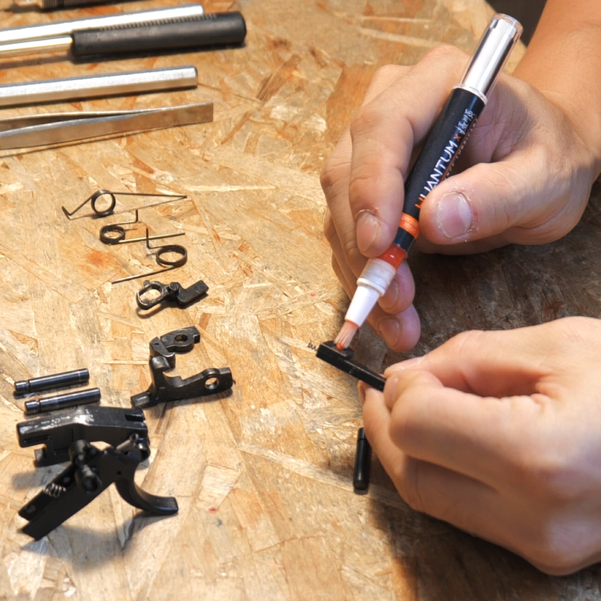 Person arbeitet mit Metallteilen und einem Stift auf einer Werkbank.