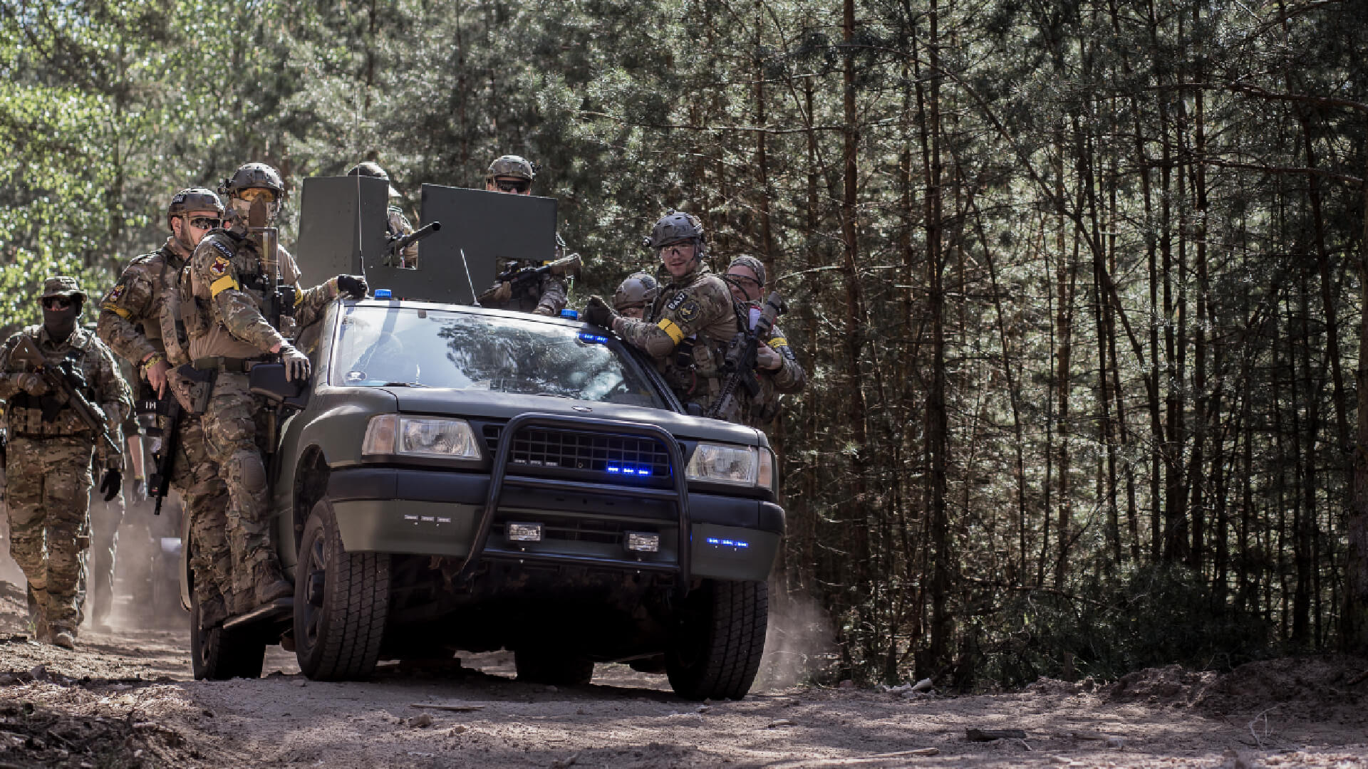 Airsoft-Team in Tarnkleidung mit Fahrzeug im Wald, bereit für ein taktisches Spiel.
