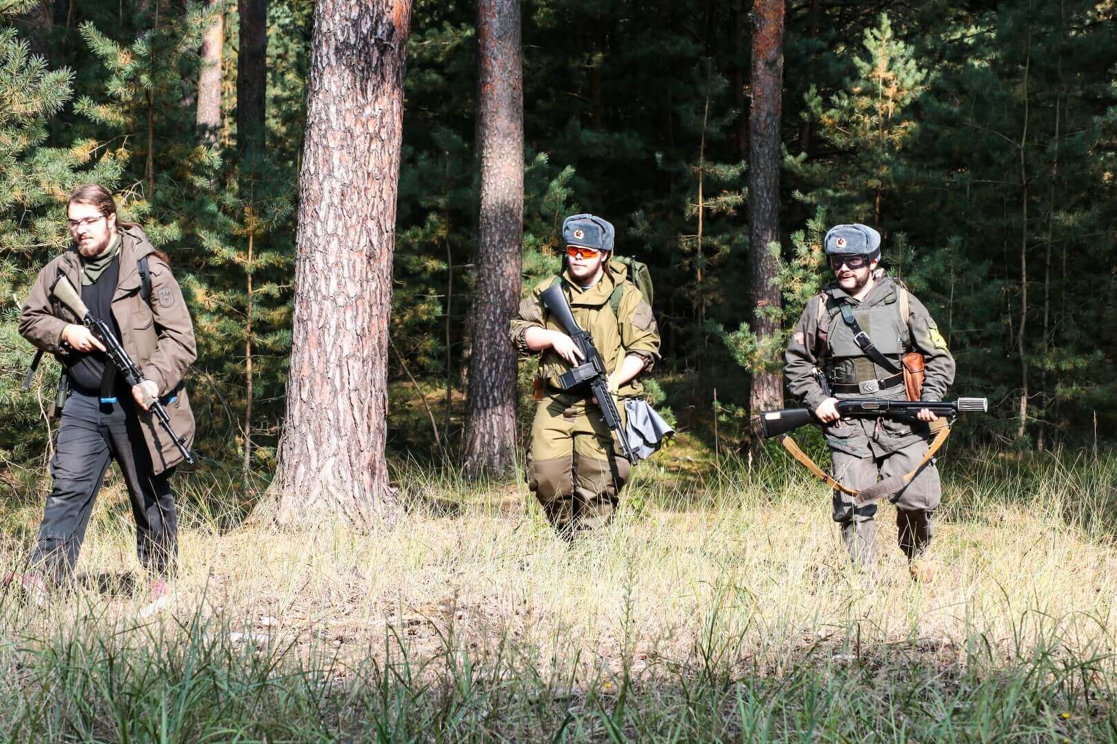 Drei Airsoft-Spieler in Ausrüstung gehen durch einen bewaldeten Bereich.