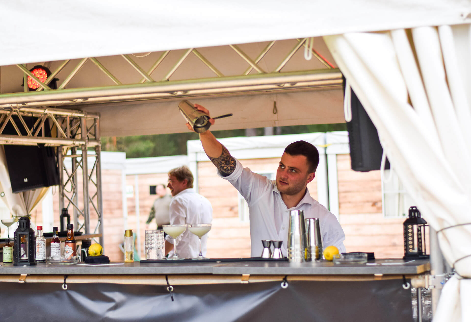 Barkeeper mixt Cocktails an einer Outdoor-Bar, umgeben von Zutaten und Shakern.