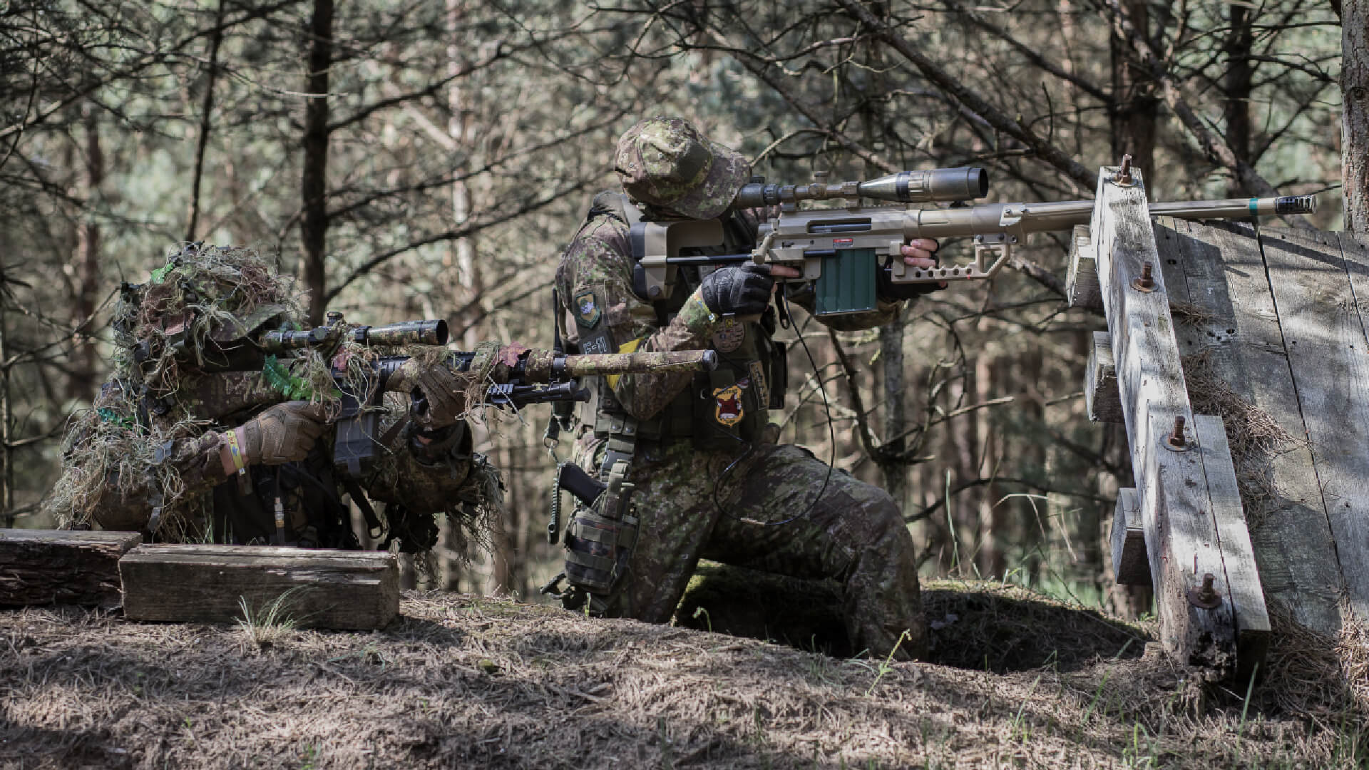 Airsoft-Spieler in Tarnkleidung zielen im Wald mit Scharfschützen- und Sturmgewehr.