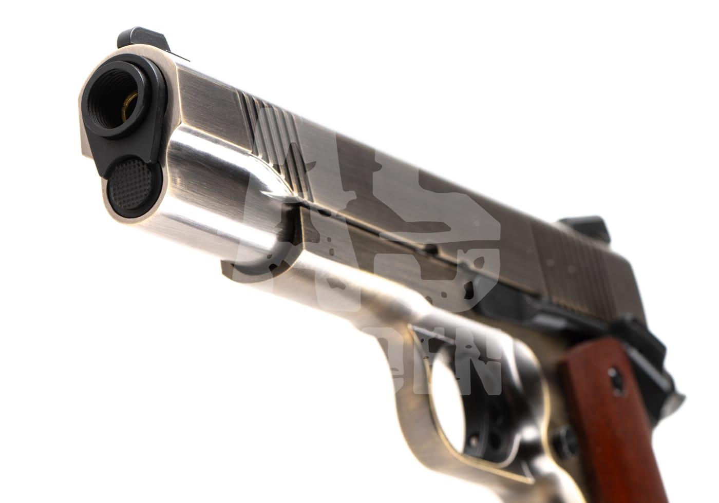 Nahaufnahme einer silbernen Airsoft-Pistole mit Holzgriff, Mündung links im Bild.