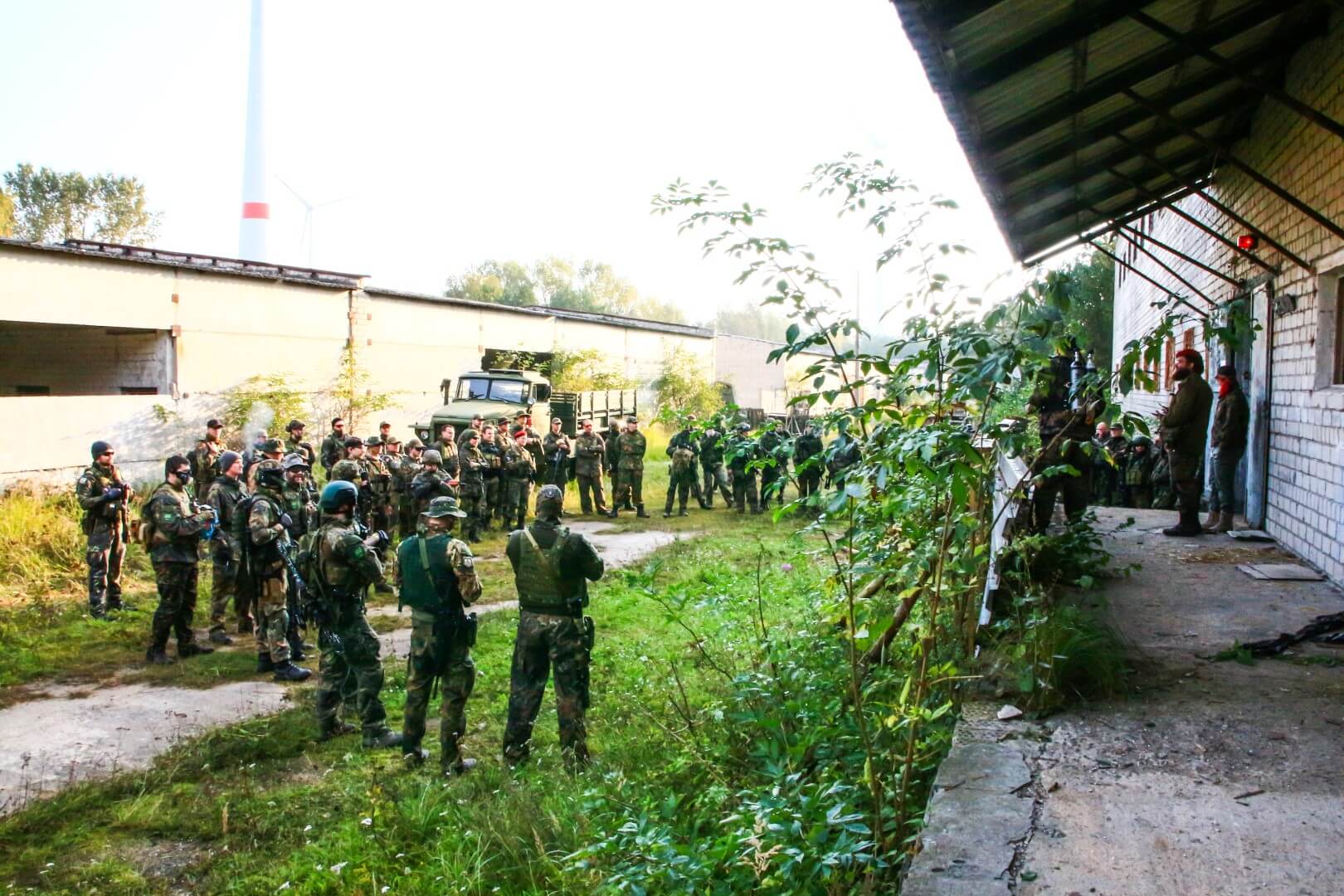 Airsoft-Spieler in Tarnkleidung versammeln sich auf einem Gelände vor einem Gebäude.