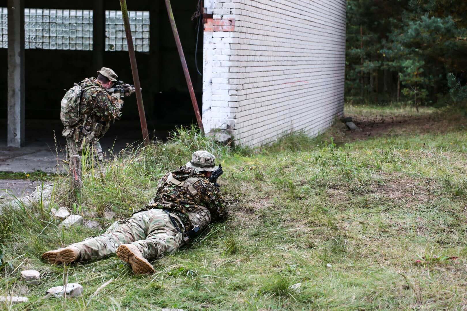 Zwei Airsoft-Spieler in Tarnkleidung bei einer Übung im Freien neben einem Gebäude.