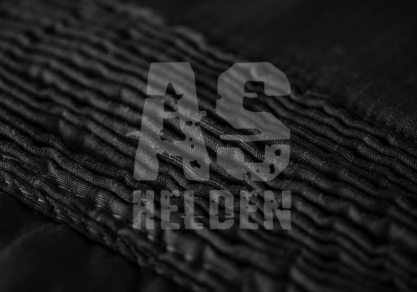 Schwarzes Texturgewebe mit „AS Helden“ Logo in Grautönen im Vordergrund.