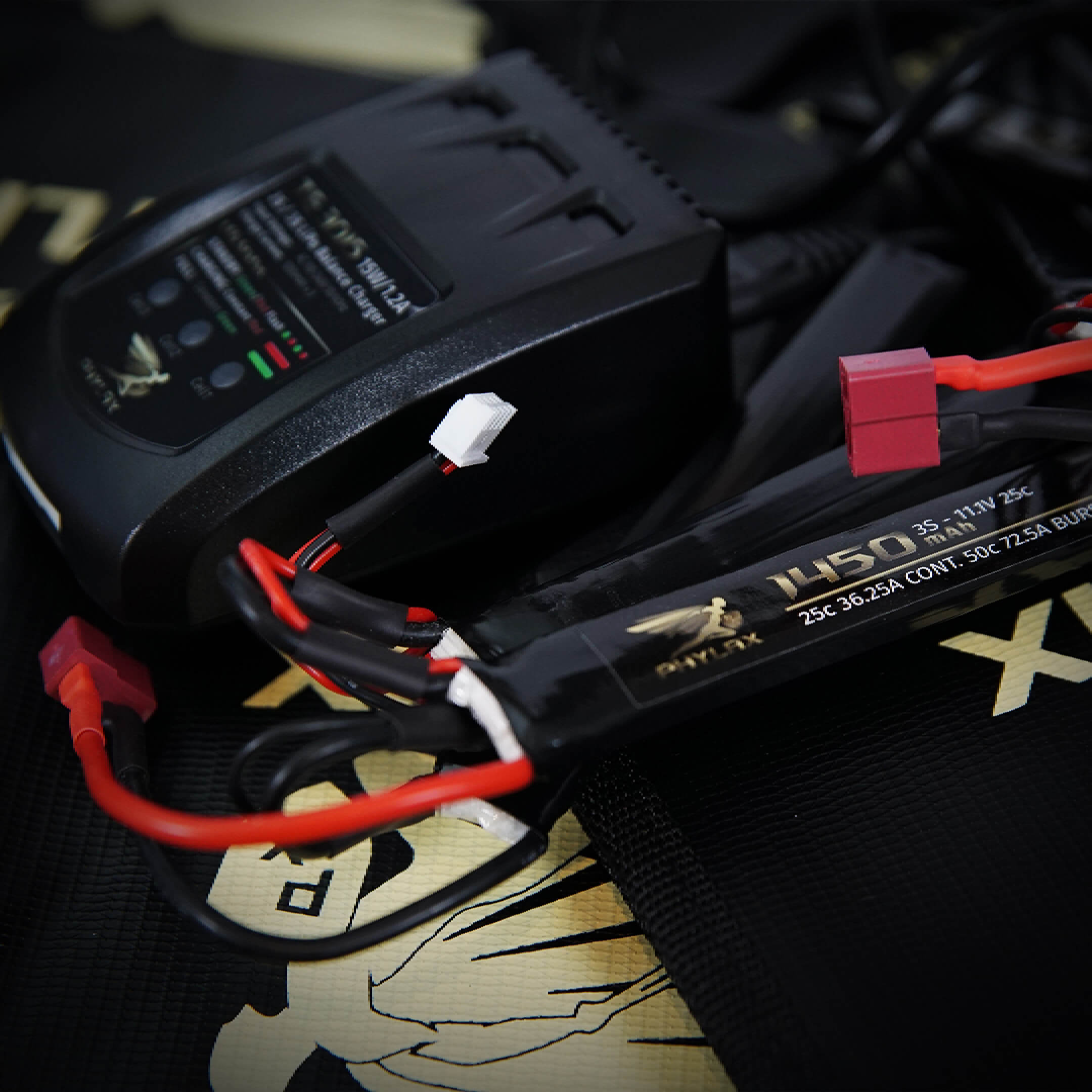 Airsoft LiPo-Akku mit Ladegerät und Kabeln auf schwarzem Untergrund.