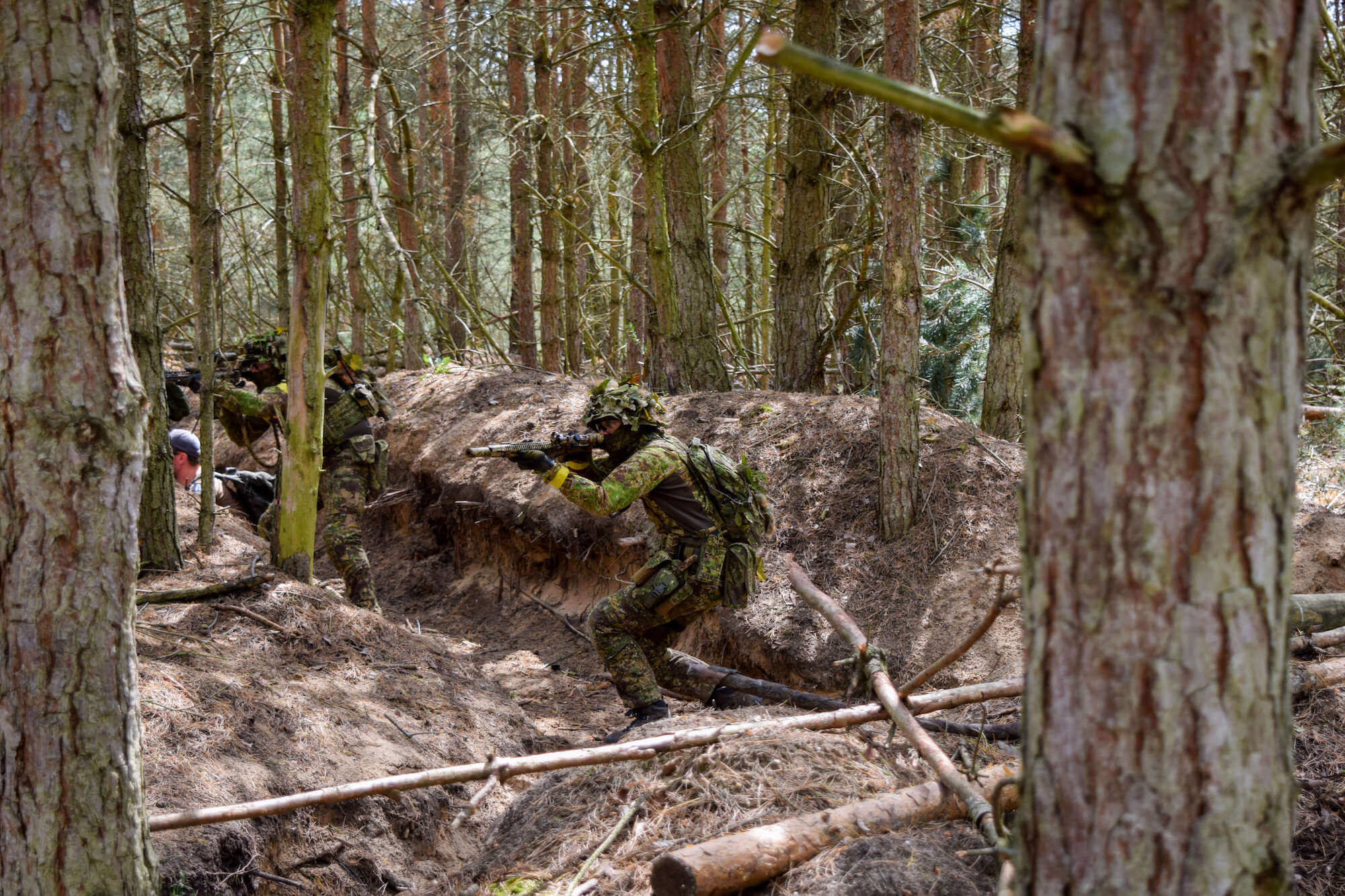 Airsoftspieler im Tarnanzug in einem Wald, kniend und zielend mit Airsoftgewehr.