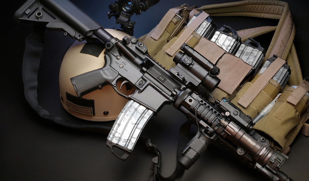 Airsoftgewehr mit Optik auf Helm, daneben Weste mit Magazintaschen, Nahaufnahme.