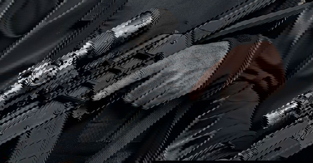 Person hält ein Airsoft-Gewehr mit Zielfernrohr, trägt eine dunkle Jacke.