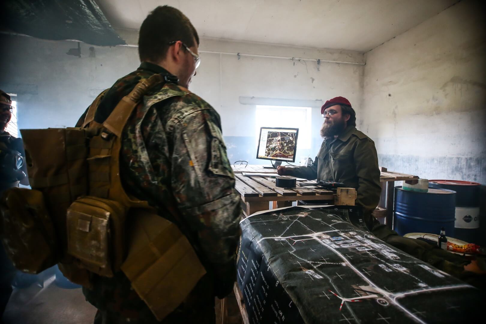 Airsoft-Spieler in Gefechtswesten besprechen Strategie an einem Tisch mit Karte und Monitor.