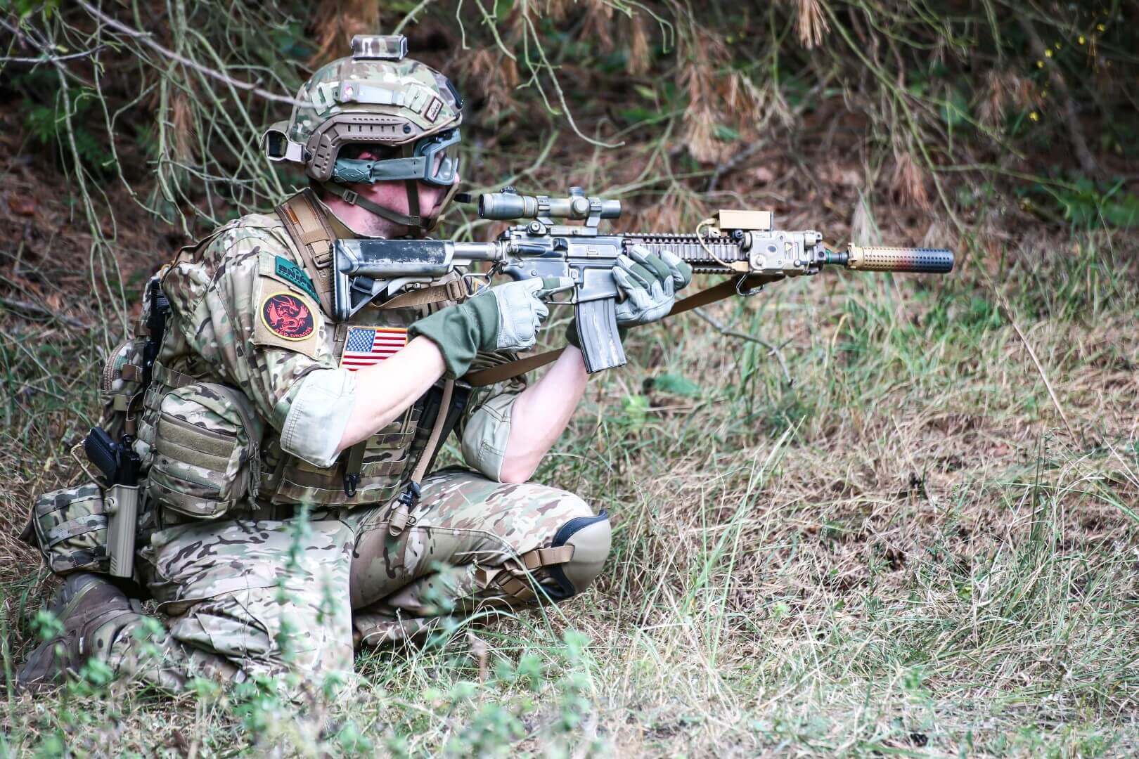 Airsoft-Spieler in Tarnkleidung zielt mit Airsoft-Gewehr im Wald.