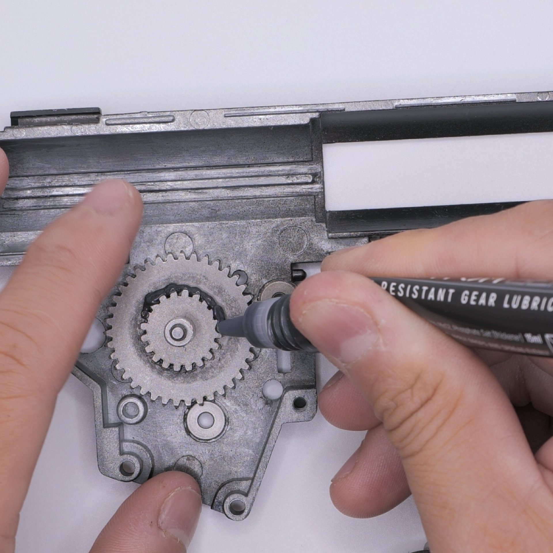 Hände schmieren ein Zahnrad mit einem Spezialstift.
