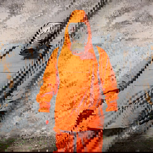 Person in oranger Schutzkleidung und Gasmaske in industrieller Umgebung.