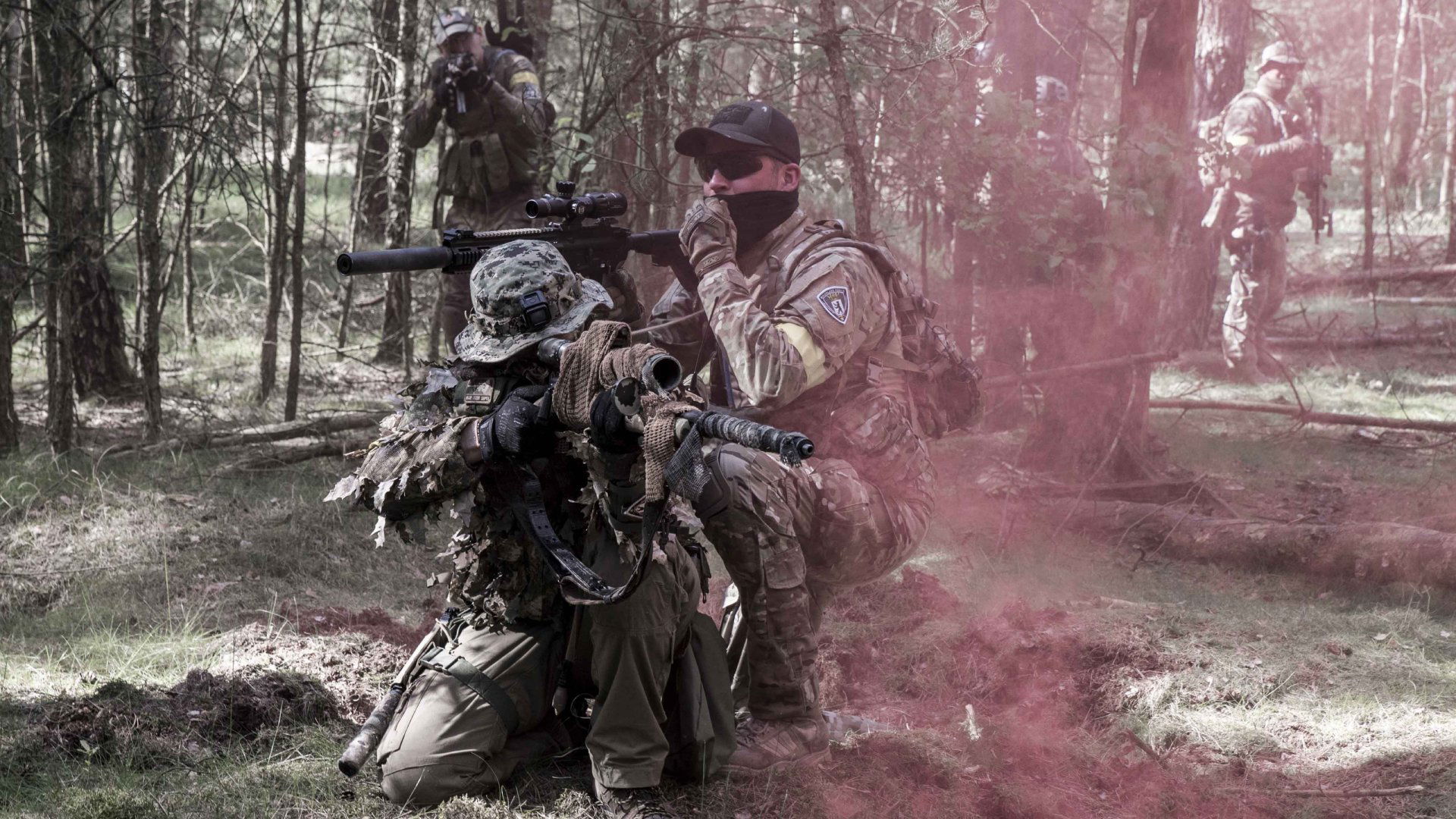 Soldaten in Tarnkleidung mit Waffen im Wald, umgeben von rotem Rauch.