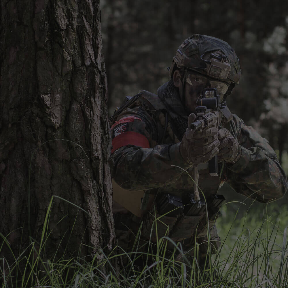 Airsoft-Spieler in Tarnung zielt hinter Baum. Outdoor-Waldkulisse.