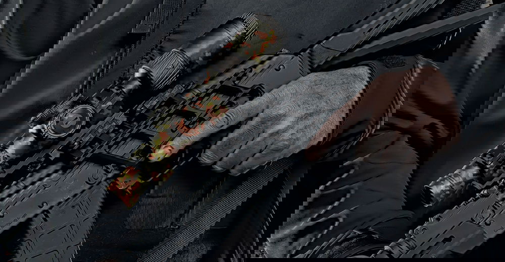 GunsWrap Scope Skins Person hält Airsoft-Gewehr mit Camouflage-Zielfernrohr, trägt schwarze Jacke.
