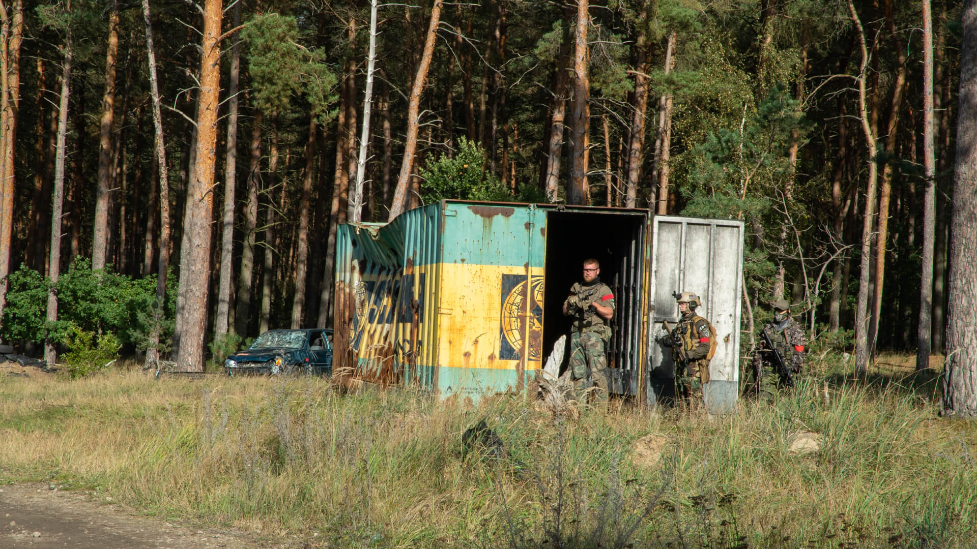Airsoft-Spieler in Tarnkleidung bei einem Container im Wald, bereit für ein Szenario.