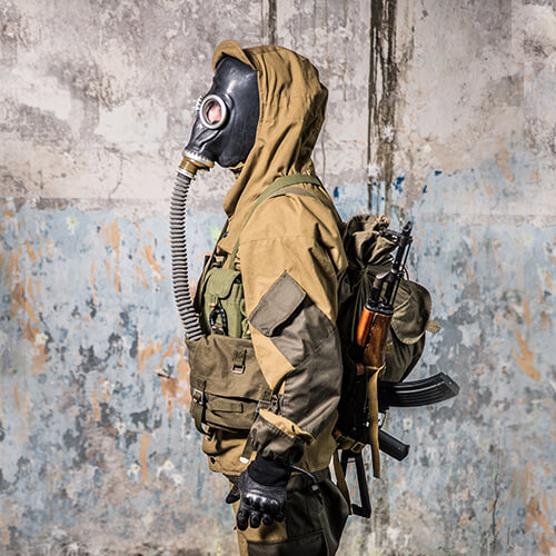 Airsoft-Spieler in Tarnanzug mit Gasmaske und Ausrüstung in urbanem Hintergrund.