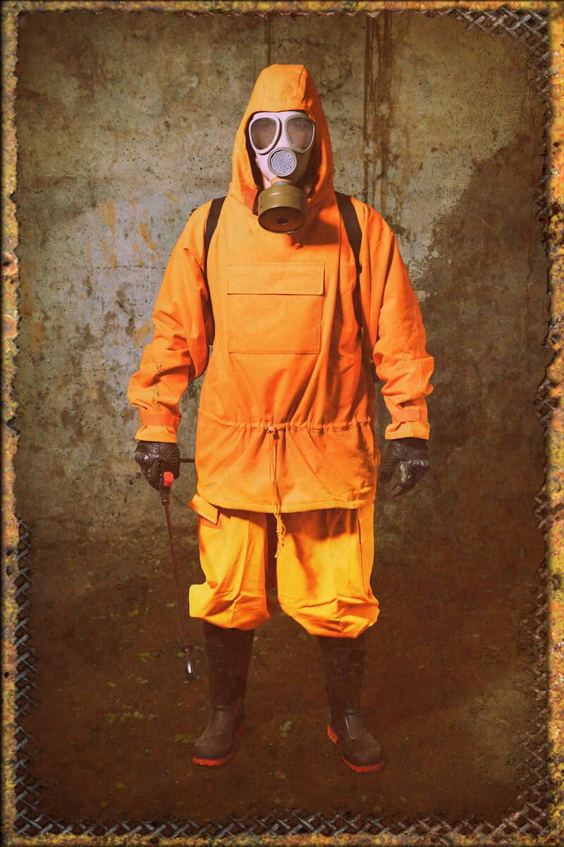 Person in orange Schutzanzug und Gasmaske, steht in industrieller Umgebung.