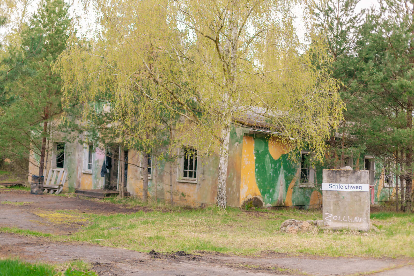 Verlassenes, getarntes Gebäude im Wald, Schild "Schleichweg" und "Zollhaus" sichtbar, ideal für Airsoft-Spiele.