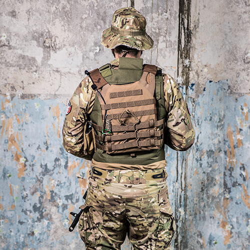 Person in Tarnkleidung und Platteweste steht vor einer Wand. Rückansicht. Perfekt für Airsoft-Ausrüstung.