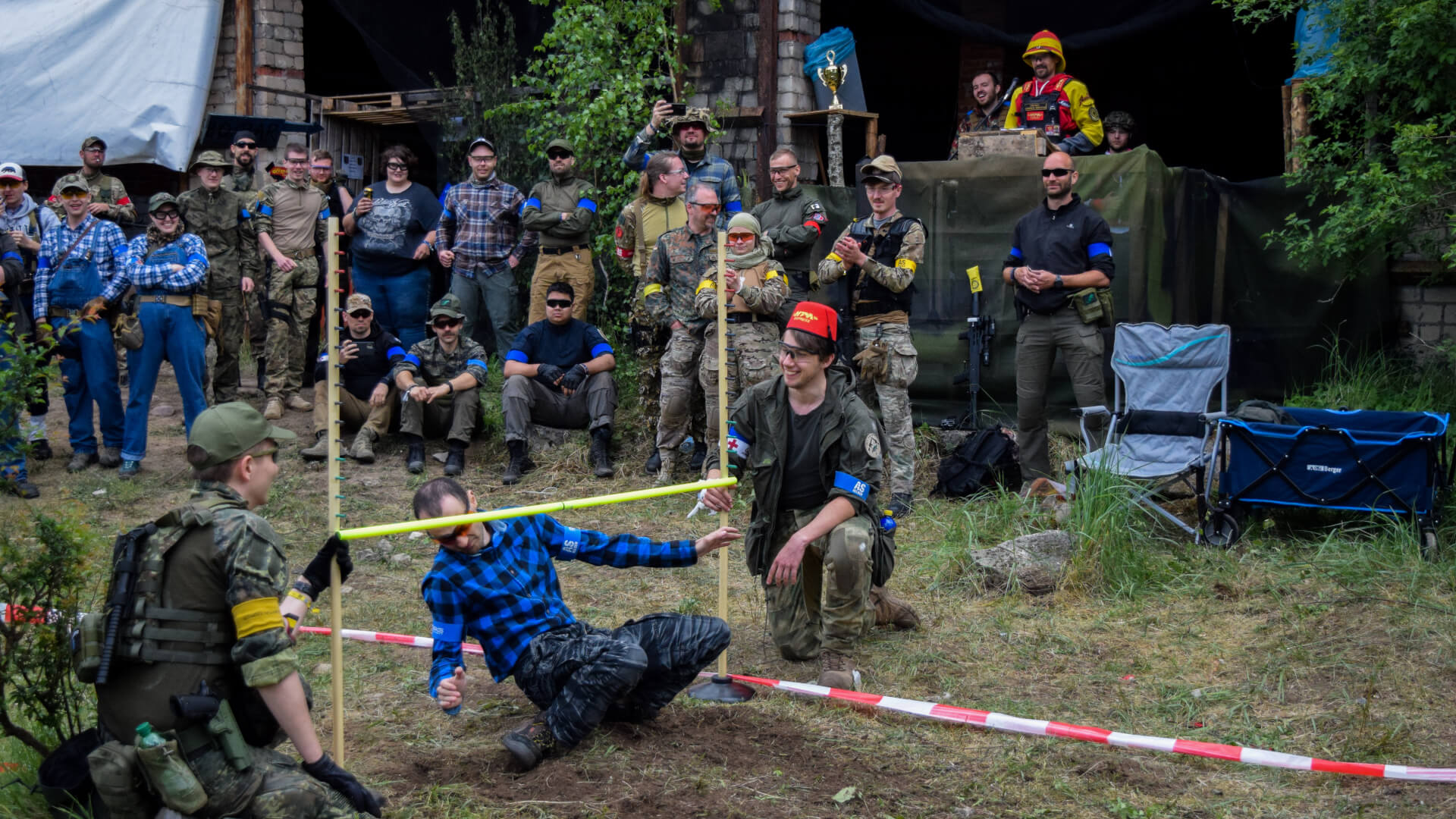 Airsoft-Event: Teilnehmer führen ein Limbo-Spiel durch, umgeben von Zuschauern in Outdoor-Kleidung.