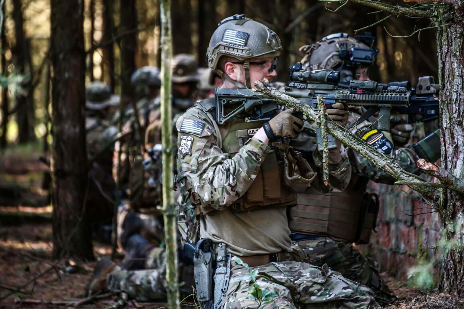 Airsoft-Spieler in Tarnkleidung zielen mit Replikas im Wald.