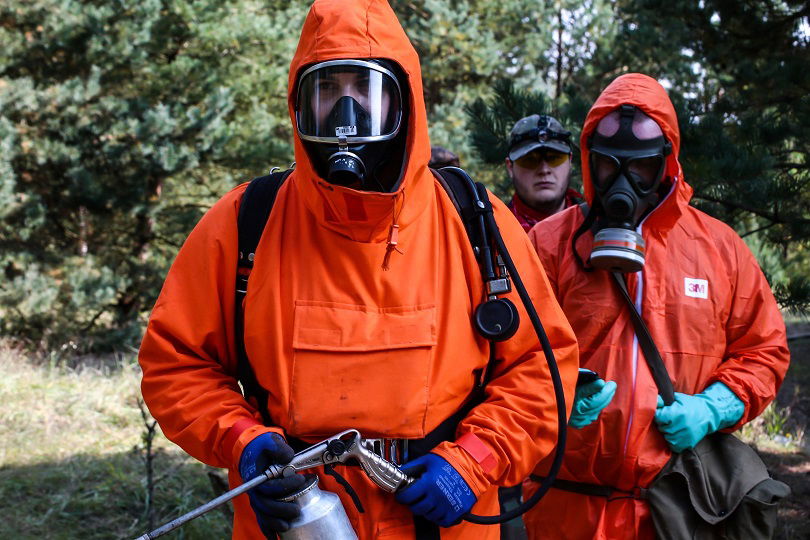 Personen in orangenen Schutzanzügen mit Atemmasken im Wald.