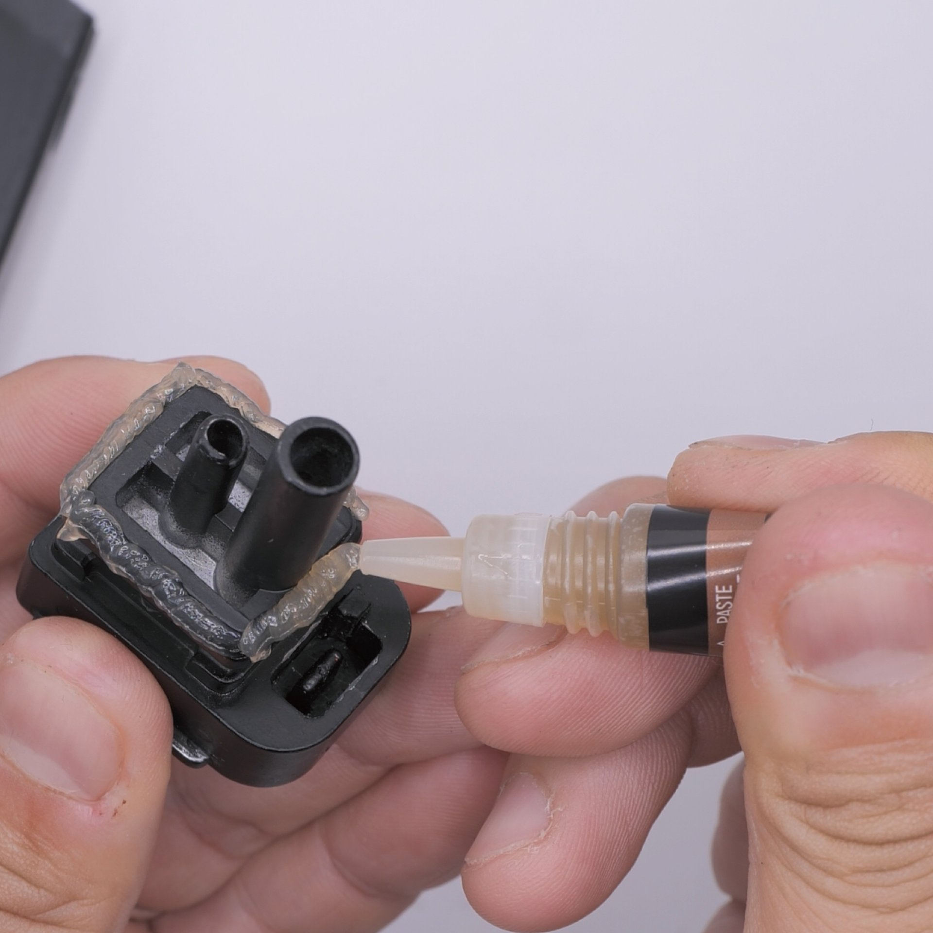 Person trägt Kleber auf ein kleines schwarzes Bauteil auf.