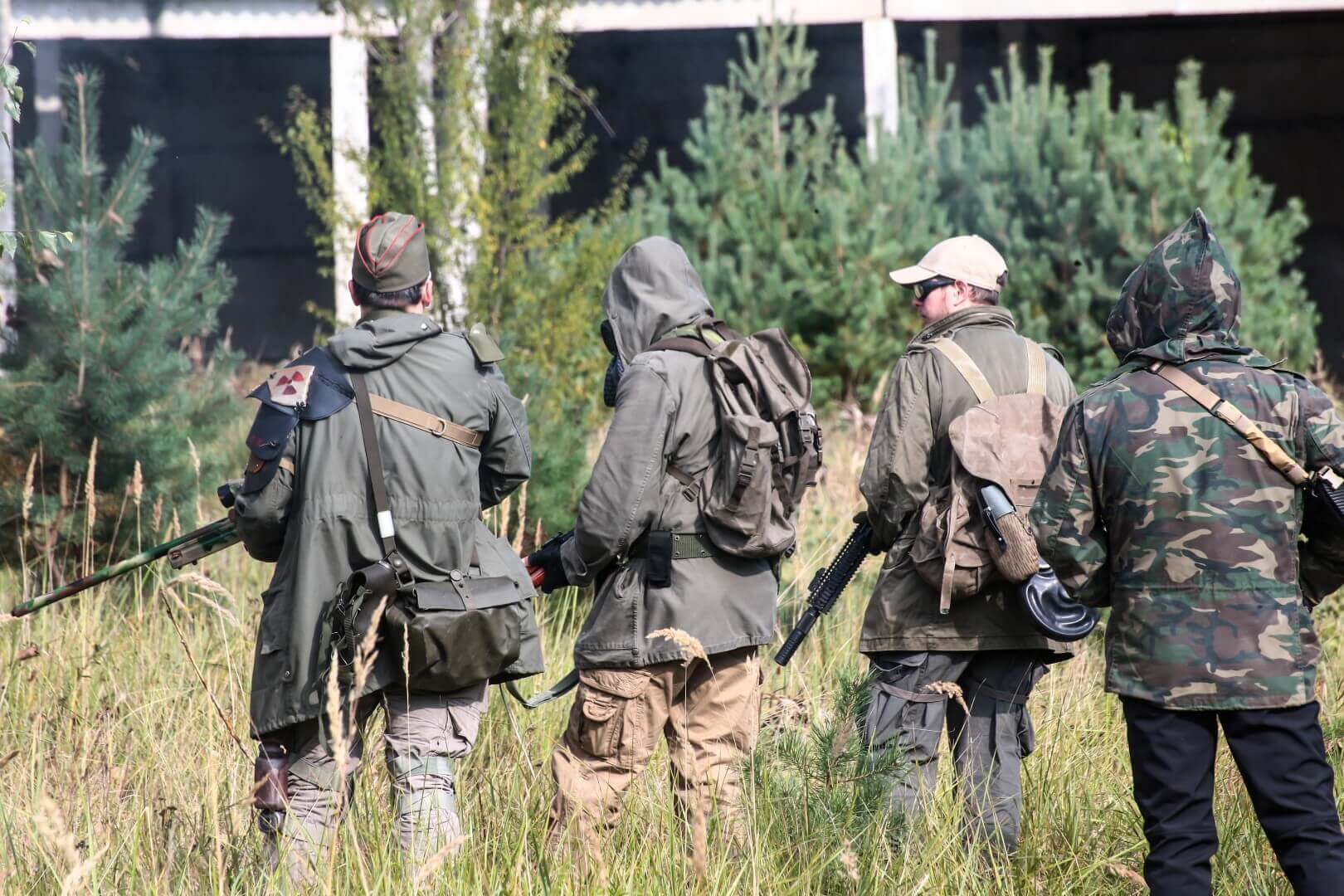 Vier Airsoft-Spieler in Tarnkleidung im Grünen, mit Ausrüstung und Gewehren.